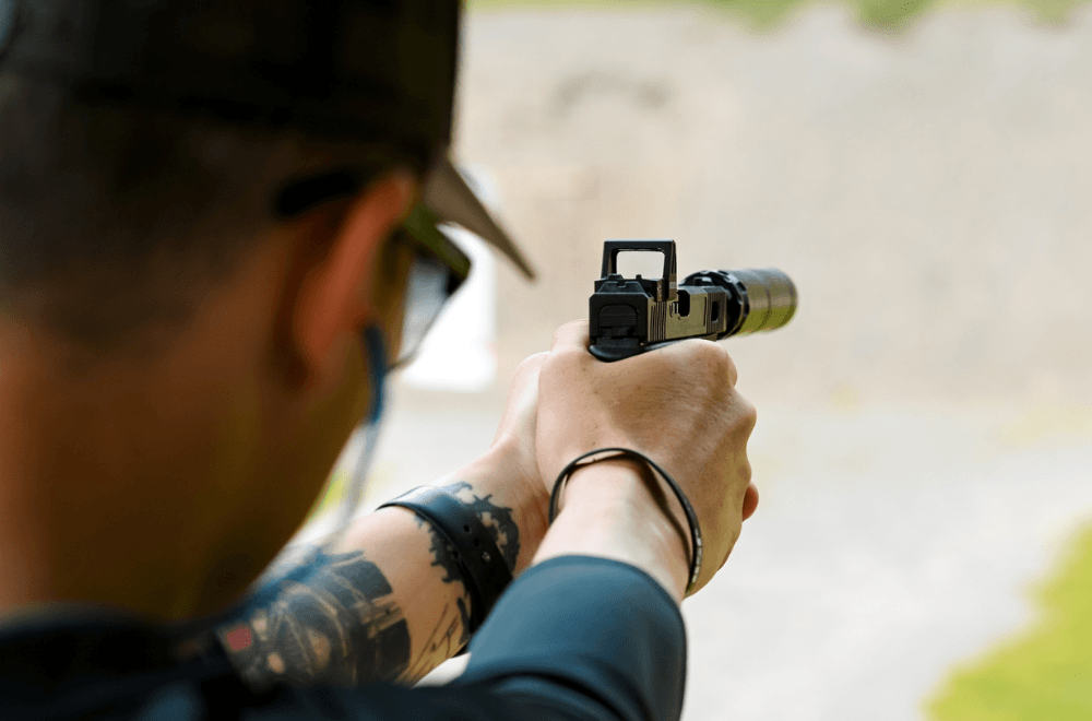 Behind the back view of a man aiming his pistol with a red dot sight mounted