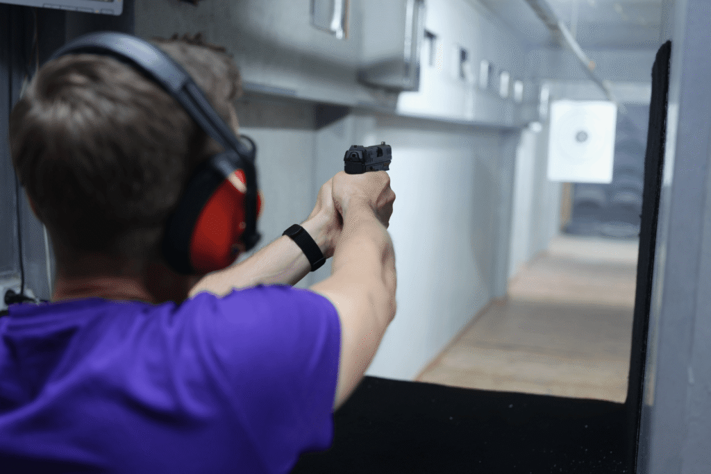 Man wearing red ear protection aiming his pistol at an indoor shooting range