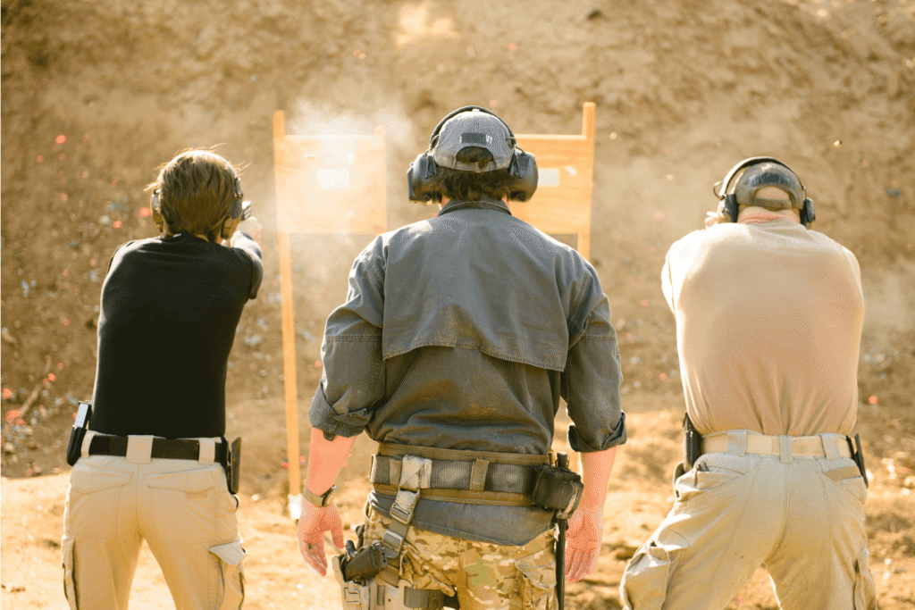 Two men firing pistols at an outdoor shooting range as the instructor watches on