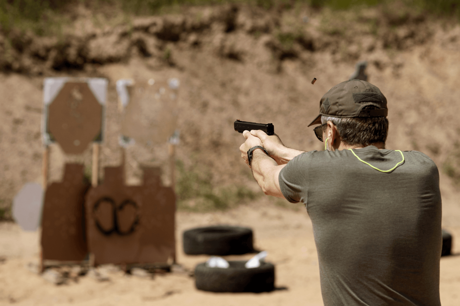Behind the back view of a man firing his pistol towards targets at an outdoor shooting range